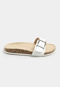 Sandalo bianco con una fascia larga e fibbia argentata, plantare in sughero, texture simile alla pelle scamosciata beige e suola in gomma bianca texturizzata.