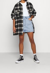 Chemise oversize à carreaux noirs et jaunes avec deux poches, t-shirt blanc moulant, mini-jupe en denim bleu et baskets montantes noires.