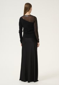 Černý svetr s síťovými rukávy a slim fit střihem, doplněný volnou černou maxi sukní. Hladká textura a bezproblémová silueta.