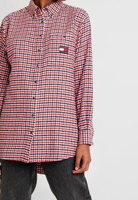 Camicia in flanella a quadri rossi e blu con chiusura a bottoni, taschino sul petto e patch del logo Tommy Jeans. Maniche lunghe e orlo curvo.
