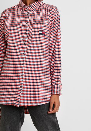Camicia in flanella a quadri rossi e blu con chiusura a bottoni, taschino sul petto e patch del logo Tommy Jeans. Maniche lunghe e orlo curvo.
