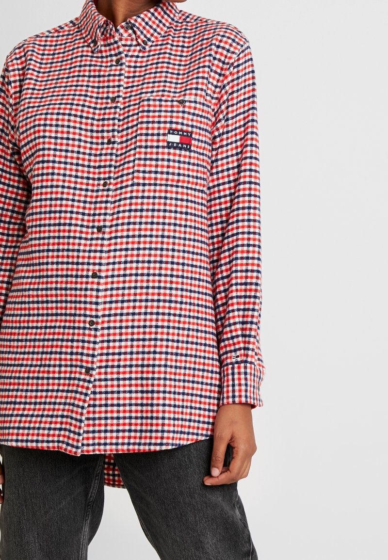 Camicia in flanella a quadri rossi e blu con chiusura a bottoni, taschino sul petto e patch del logo Tommy Jeans. Maniche lunghe e orlo curvo.