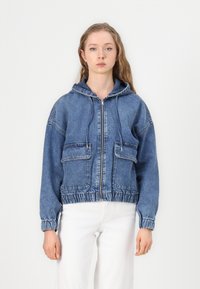 Jeans jakna s kapuljačom, s patentnim zatvaračem sprijeda, dva velika džepa, elastični završetak i manšete, u srednjoj plavoj boji.