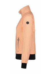 Kevyt persikkavärinen takki, jossa on korkea kaulus, vetoketjulliset sivutaskut ja musta logo-patch vasemmassa hihassa. Varustettu elastisilla hihansuilla.