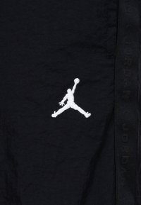 Shorts neri in tessuto con logo Jumpman ricamato bianco. Pannello laterale con testo "JORDAN" nero. Materiale testurizzato.