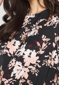 Black floral blouse featuring pale pink and burgundy flowers, round neckline, and flowing fabric with a smooth texture.