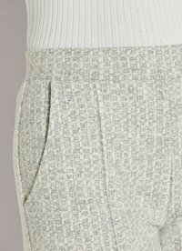 Close-up van grijs en witte textuur broek met voorplooien en zijzakken, gedragen met een wit geribd topje.