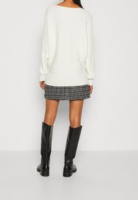 Bílý žebrovaný svetr s volným střihem, doplněný černo-bílou vzorovanou sukní. �Černé kozačky až ke kolenům doplňují outfit.