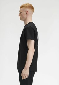 T-shirt nera in cotone con colletto tondo e maniche corte, caratterizzata da un dettaglio grafico bianco sul retro. Design semplice, vestibilità regolare.