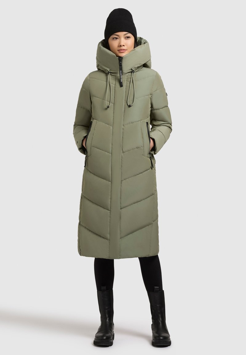 Polstret långjacka i olivgrön med hög krage, dragkedjestängning, sidfickor och sicksackmönster. Bärs med svarta leggings och stövlar.
