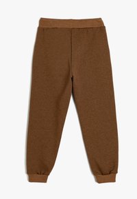 Bruine joggingsbroek met een elastische tailleband, taps toelopende boorden en een zachte textuur. Naaddetails lopen verticaal langs de achterkant.