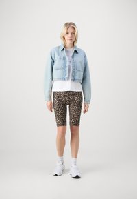 Giacca di jeans blu chiaro corta sopra una t-shirt bianca, abbinata a pantaloni corti da ciclismo con stampa leopardata marrone e sneakers bianche. Design semplice e vestibilità casual.