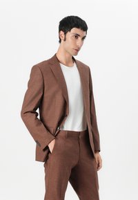 Hnedý textúrovaný oblek so slim fit strihom, single-breasted blejzerom a zladenými nohavicami, doplnený bielym tričkom.