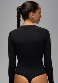 Bodysuit noir à manches longues, fabriqué dans un matériau lisse avec un design ajusté et une taille haute, mettant en valeur un décolleté plongeant dans le dos.