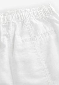 Un tessuto leggero bianco con una vita elasticizzata arricciata, dotato di una tasca posteriore e una superficie liscia e strutturata.