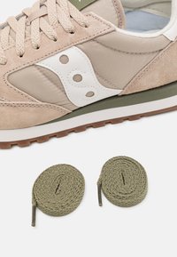 Beige atletik sko med overdel i semsket skinn og stoff, hvitt logo og grønne detaljer. To olivengrønne, runde skolisser vist under skoen.