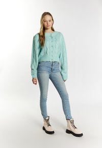 Ljusblå stickad cardigan med kabelmönster, som har knappar och ballongsärmar, kombinerad med ljusa jeans och beige snörstövlar.