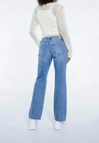 Lehký pletený top s dlouhým rukávem v bílé barvě, kombinovaný s vysokými, širokými modrými džínami, které mají dvě zadní kapsy a surový lem.