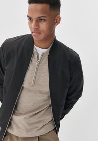 Must musta bomberjope lukuga ja soonikkoelusega kraega, kantud beeži henley-särgi peal. Sile kangas, vaba lõige ja detailne õmblustus.