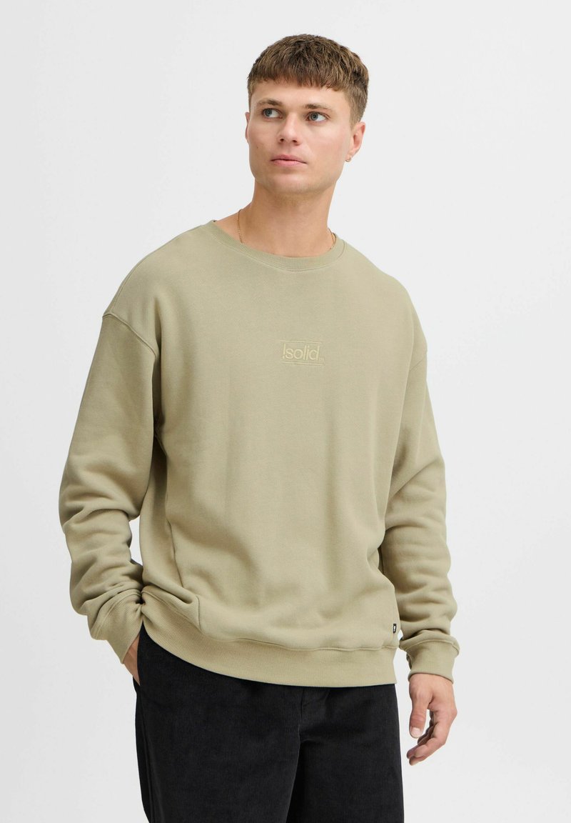 Sudadera de cuello redondo verde oliva, hecha de una tela suave, con un logotipo tonal sutil en la parte frontal, corte relajado y puños acanalados.