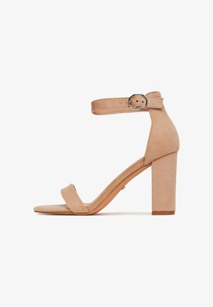 Sandalo con tacco a blocco in camoscio beige con cinghietta alla caviglia e dettaglio fibbia. Presenta una suola piatta e un design minimalista.