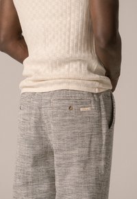 Débardeur en tricot beige avec des côtes verticales, associé à un pantalon texturé gris avec poches arrière et détail de bouton.