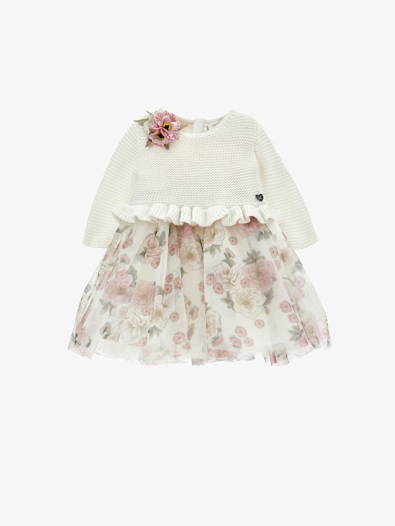 Baltā adītā garā piedurkne topā ar viļņotu apakšmalu, apvienots ar ziedu tilla svārkiem, kuros ir rozā un krēms ziedi. Akcentēts ar ziedu.