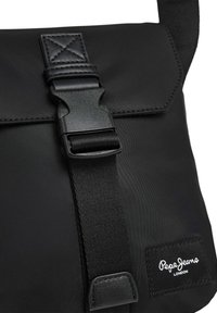 Borsa a tracolla nera realizzata in nylon liscio, con una chiusura a fibbia in plastica prominente, tracolla regolabile e un piccolo logo bianco.