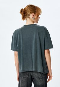 Czarna szara, oversize t-shirt z krótkimi rękawami. Miękka tekstura, okrągły dekolt, opadające ramiona. Połączona z czarnymi dżinsami o wysokim stanie.
