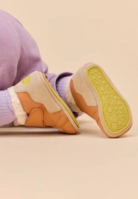Botines en tonos marrón claro y beige con una parte superior suave y texturizada, y suelas de goma que presentan un patrón de adherencia amarillo. Forro acogedor alrededor del tobillo.