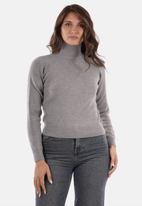 Maglione a collo alto grigio a coste con maniche lunghe, caratterizzato da un design aderente e un tessuto testurizzato, abbinato a jeans in denim scuri.