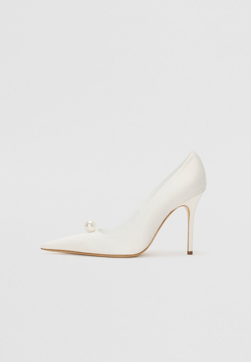 Pantofii cu toc înalt, vârful ascuțit, de culoare albă, cu un finisaj lucios, având un accent decorativ din perlă pe lateral și un toc subțire de tip stiletto.