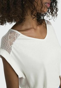 Biała bluzka z krótkim rękawem i dekoltem w kształcie litery V, z koronkowymi wstawkami na ramionach oraz miękkim, teksturowanym materiałem.