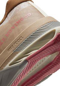 Gros plan de la semelle beige et rose d'une chaussure de sport avec un design texturé et rainuré et un marquage partiel "Nike React" visible.