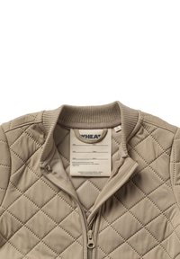 Beżowa pikowana kurtka na zamek błyskawiczny z prążkowanym kołnierzem, z metką wewnątrz, na której można wpisać imię i ulubione miejsce do ukrycia się.