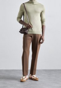 Světlý zelený rolák, hnědé na míru šité kalhoty, hnědá kabelka přes rameno a vícebarevné tenisky s růžovými a bílými akcenty.