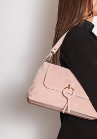 Blush roze, suède handtas met een vlak ontwerp, een bovenklep en een gouden metalen ringaccent. Voorzien van een afneembare schouderband.