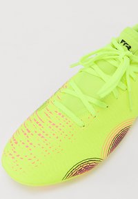 Bright yellow soccer shoe with a textured upper, features pink and black graphic patterns, and green laces. Rounded toe shape, lightweight design.
