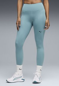 Ανοιχτό μπλε αθλητικό κολάν με ψηλό ύψος μέσης και ραμμένα σχέδια, συνδυασμένο με λευκά αθλητικά παπούτσια και ριμπ κάλτσες με λογότυπο.