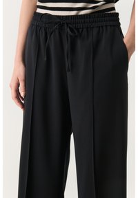 Pantalons larges noirs avec une taille élastique et un cordon de serrage, dotés de poches latérales et d'une texture douce et lisse.