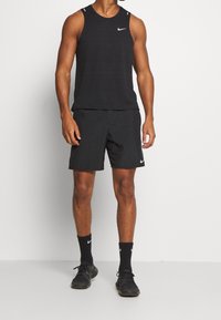 Camiseta sin mangas negra de Nike con textura horizontal, combinada con pantalones cortos negros. Presenta un pequeño logotipo blanco de Nike en el pecho y en la pierna.