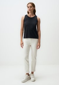 Top senza maniche di colore nero realizzato in tessuto morbido, abbinato a jeans bianchi aderenti e sneakers bianche. Design semplice, senza motivi o dettagli visibili.