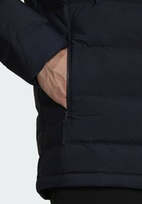 Giacca puffer blu navy con tasca laterale con zip. Il materiale appare liscio e trapuntato, offrendo isolamento e calore.