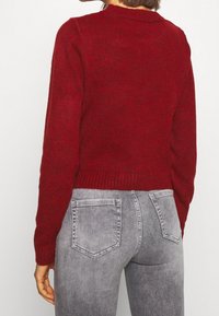 Un pull en tricot rouge avec un col rond, des poignets et un ourlet côtelés, associé à un jean en denim gris avec des poches arrière et une texture délavée.