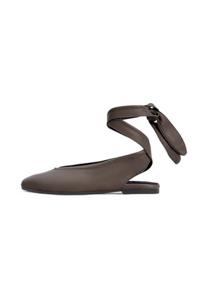 Zapato plano de cuero marrón con punta afilada y tira que rodea el tobillo atada con un lazo sobre un fondo blanco.