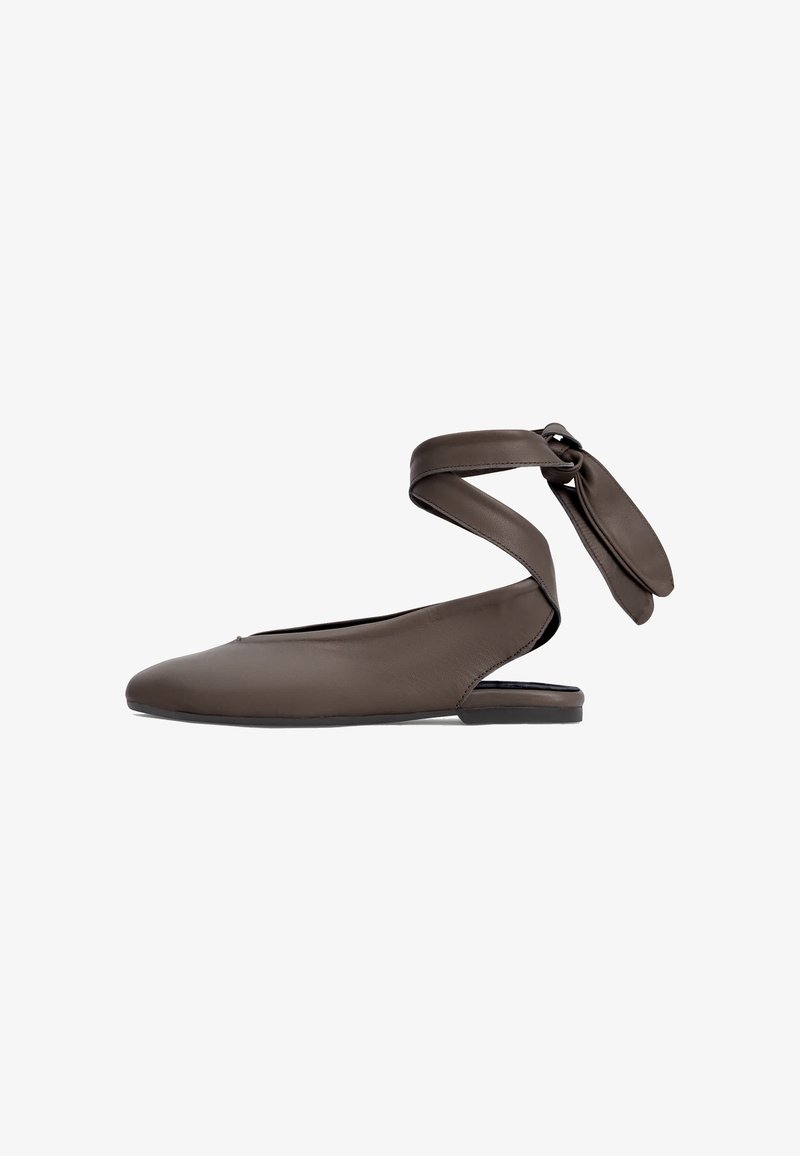 Chaussure plate en cuir marron avec bout pointu et bride à la cheville nouée en nœud sur fond blanc.