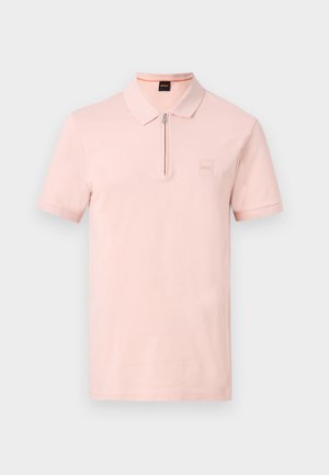 Ανοιχτό ροζ πόλο με κοντά μανίκια, φερμουάρ στη γιακά και διακριτικό λογότυπο της μάρκας στο αριστερό στήθος πάνω σε μονόχρωμο φόντο.