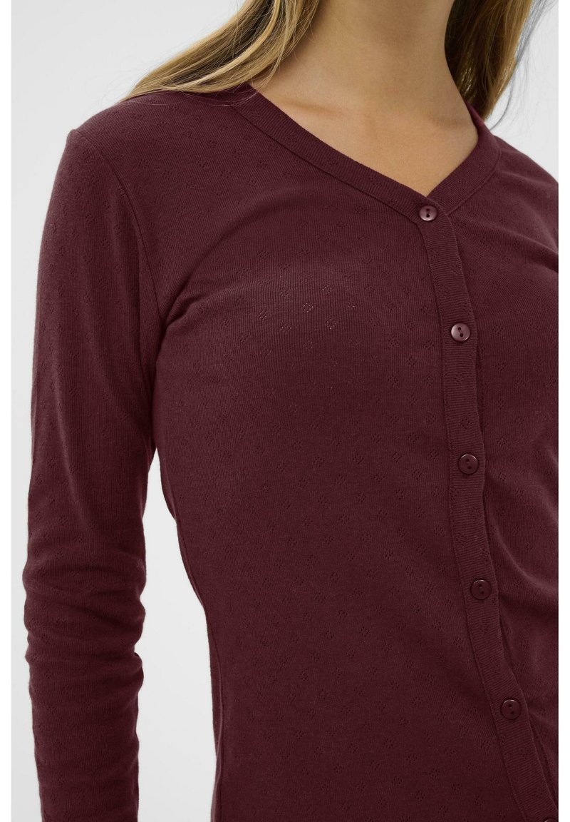 Burgundy långärmad cardigan med V-hals, strukturerat tyg och dekorativa knappar längs framsidan, med en figurnära passform.