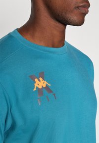 Blauwe katoenen t-shirt met een ronde hals en korte mouwen, voorzien van een grafisch logo in oranje en donkergrijs op de voorkant.