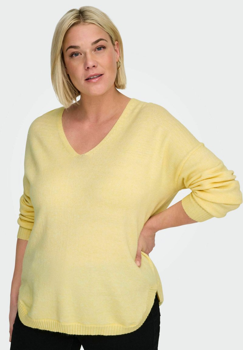 Pull jaune à col en V en tissu doux, avec manches longues, coupe décontractée, fentes latérales et détails de bord-côte à l'ourlet.